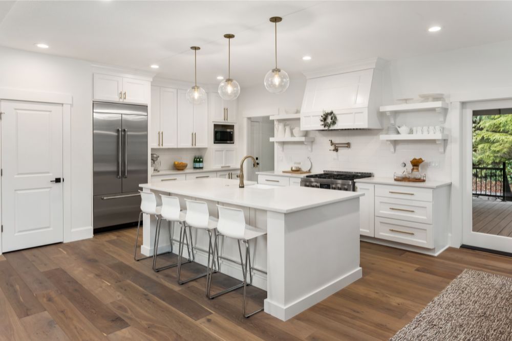 Bright white kitchen with a large island, stainless steel appliances, and wooden floors.