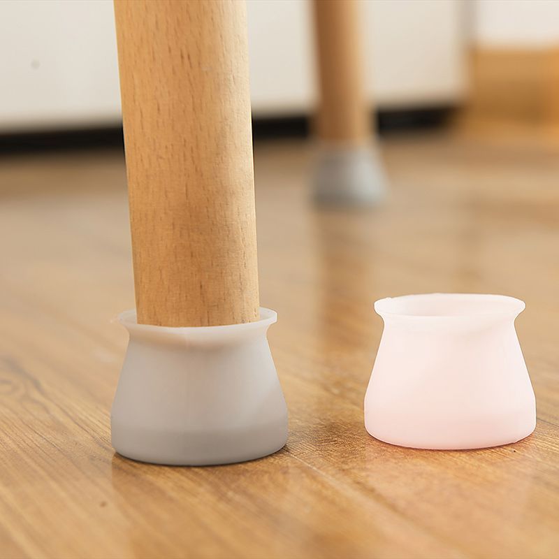 Light brown wooden chair legs with gray and pink silicone leg covers on a wood floor.