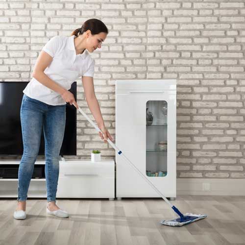 Woman mopping a wooden floor in a living room with a white cabinet and TV.