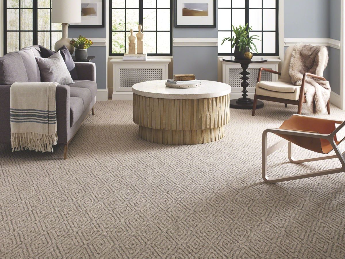 Living room with beige patterned carpet, gray sofa, round wooden coffee table, and an armchair.