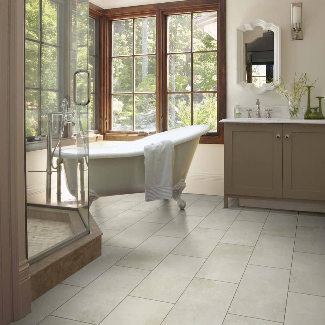 Bathroom with freestanding tub, stone tile floor, and large window overlooking trees.