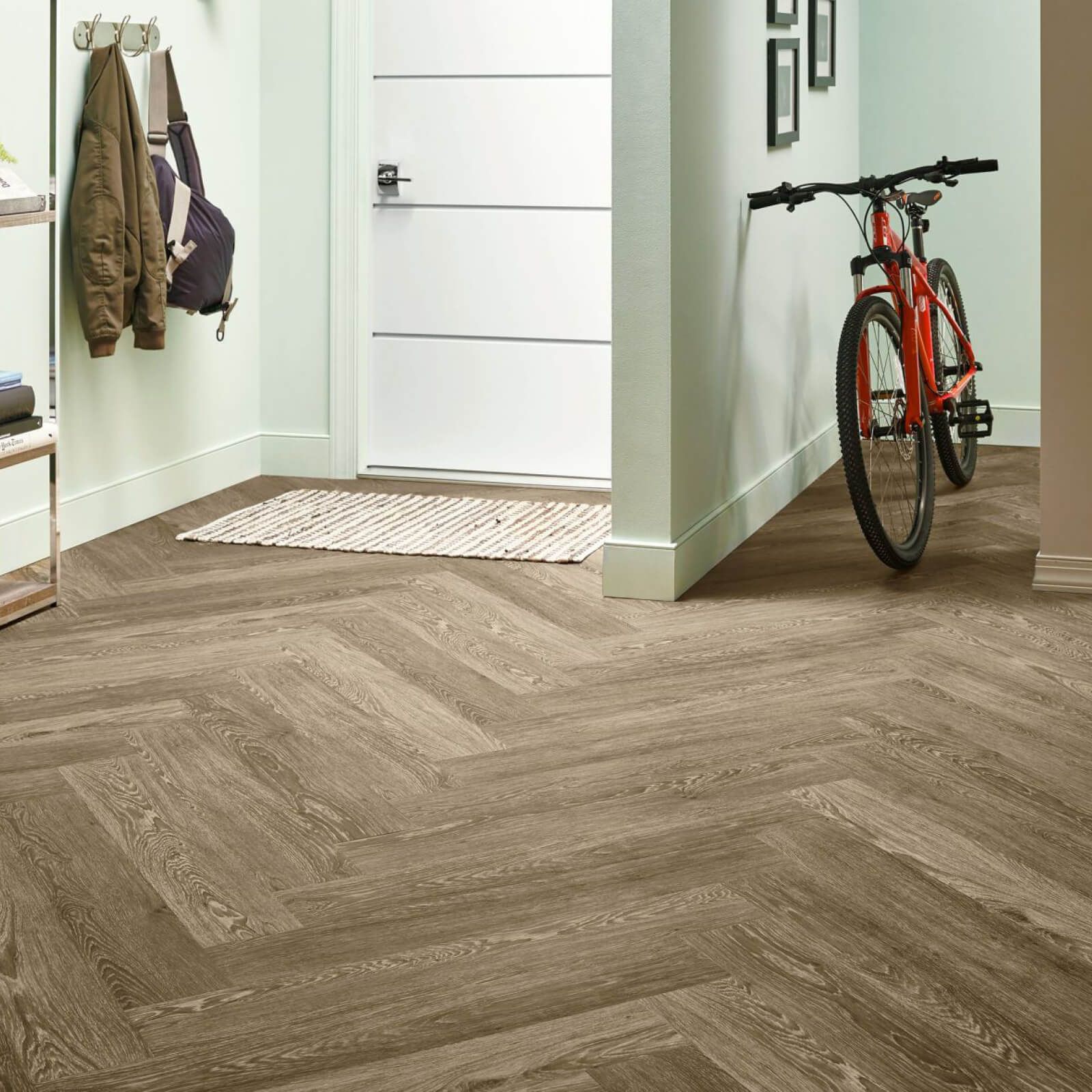 Entryway with herringbone wood-look floor, coat rack, white door, bicycle leaning against the wall.