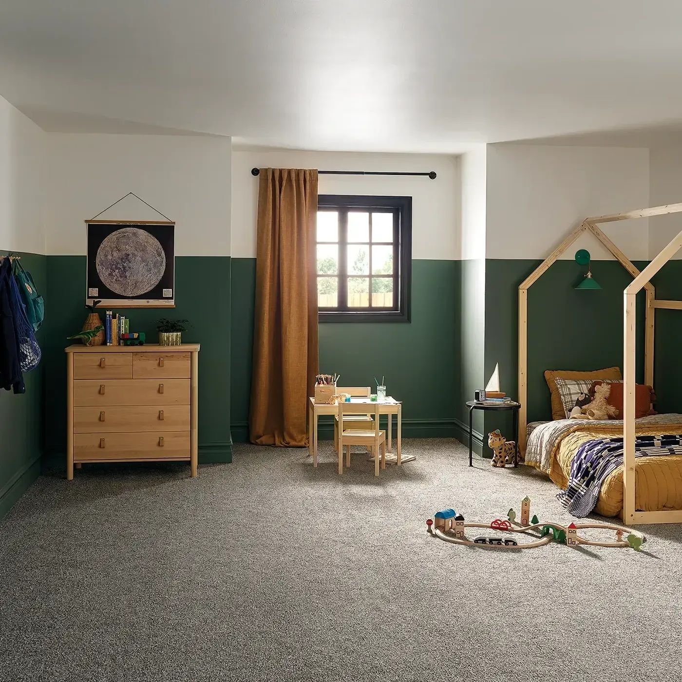 Child's bedroom with green and white walls, wood bed frame, rug, small table/chairs, wood chest.