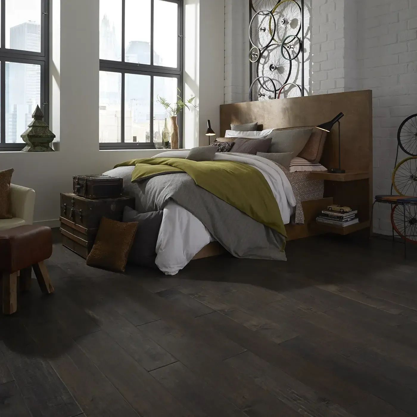 Bedroom with dark wood floor, large windows, bed with headboard, and bicycle wheel art.