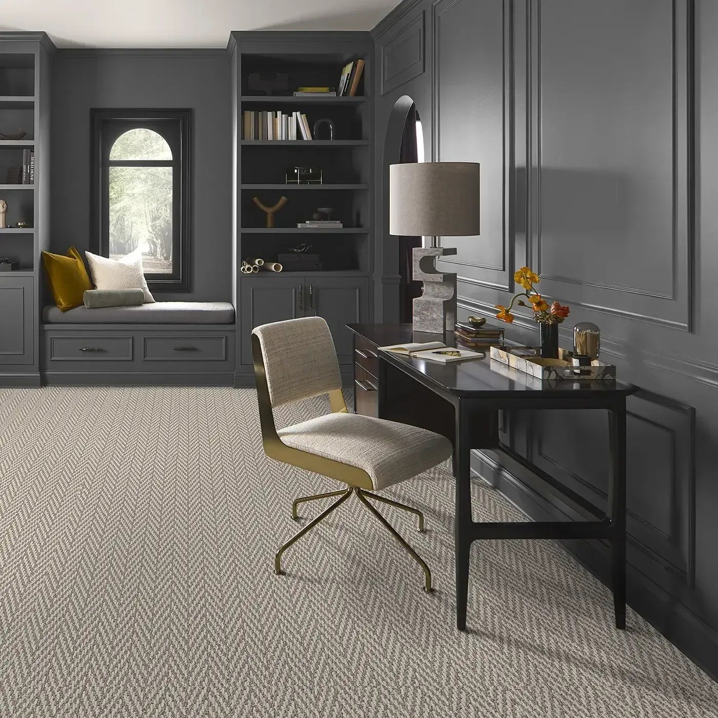 Gray home office with desk, built-in shelves, window seat, and neutral patterned carpet.