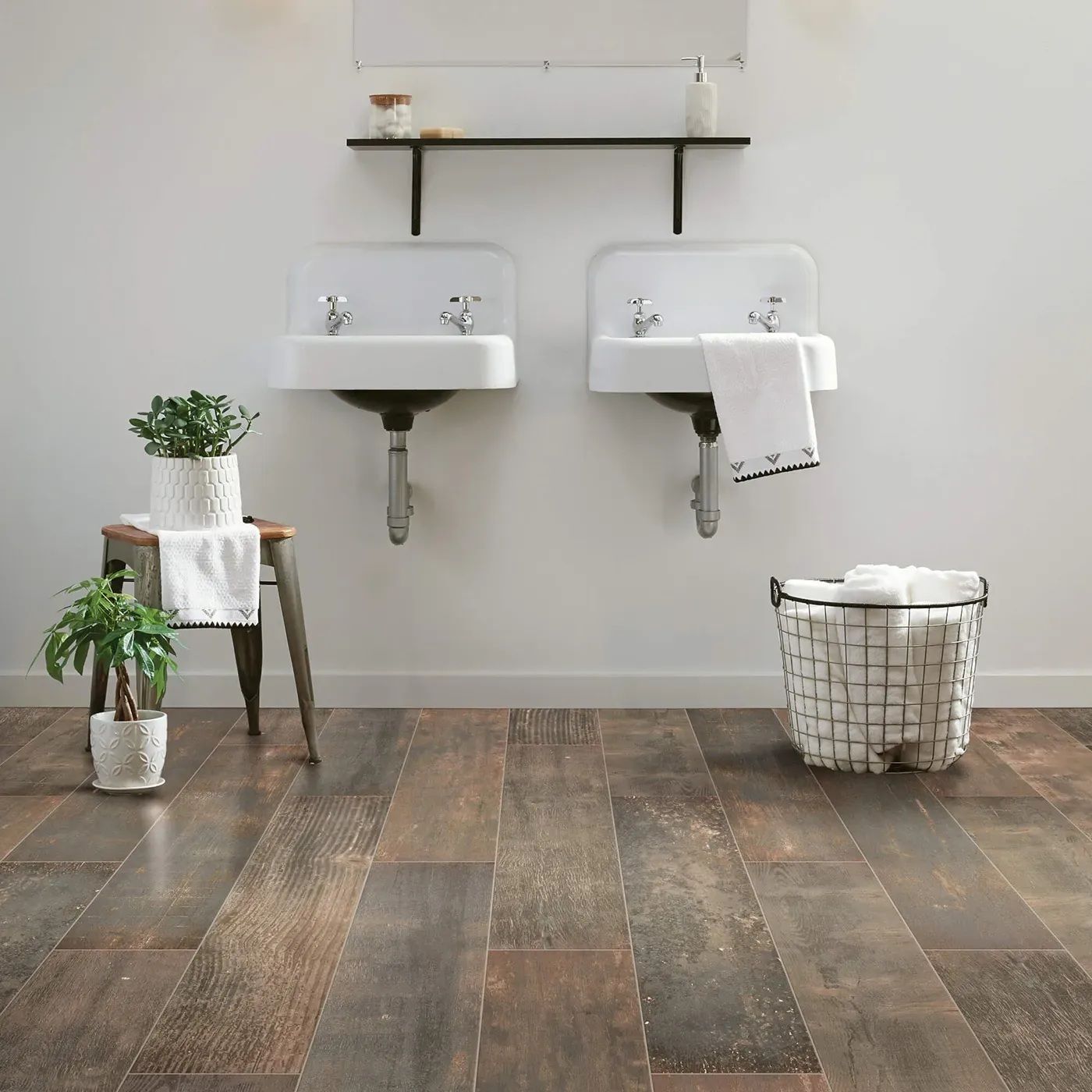 Bathroom with two white sinks, wooden floor, towels, plants, and a basket.
