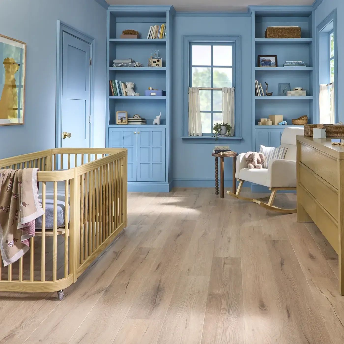 Blue nursery with wooden crib, shelves, dresser, and light wood flooring.