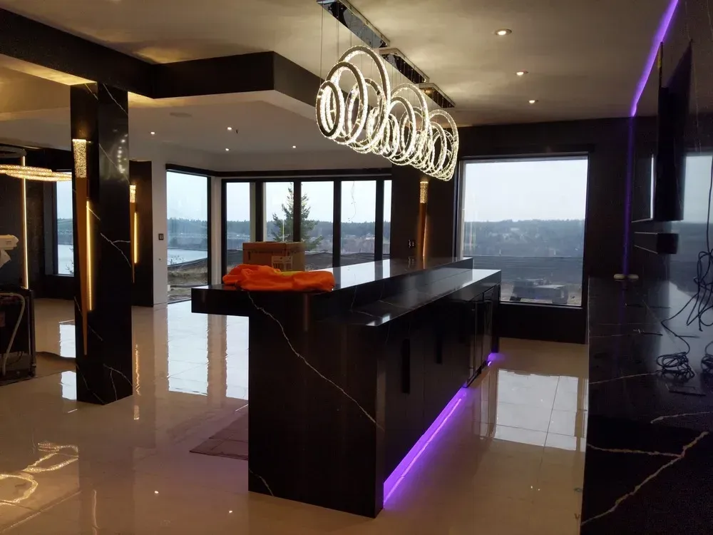 Modern luxury kitchen with black island, purple lighting, and city view through large windows