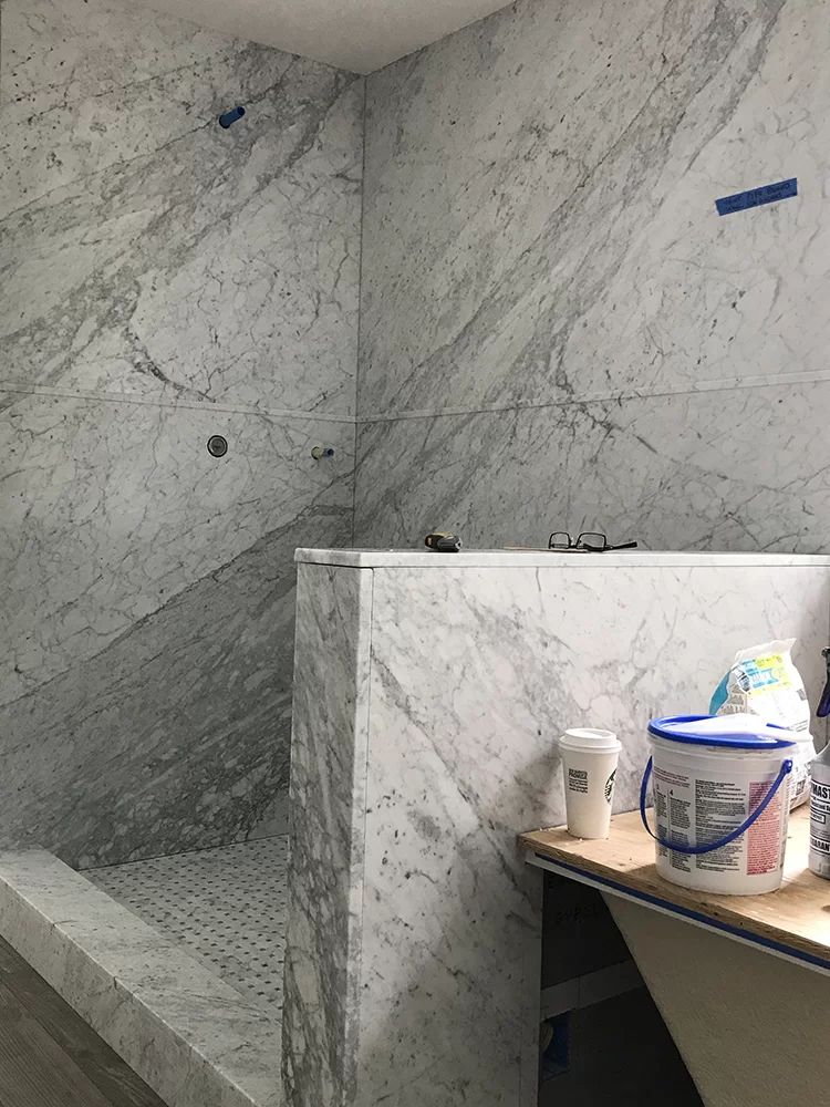 Marble-tiled shower stall under construction with a half wall and a work table holding supplies