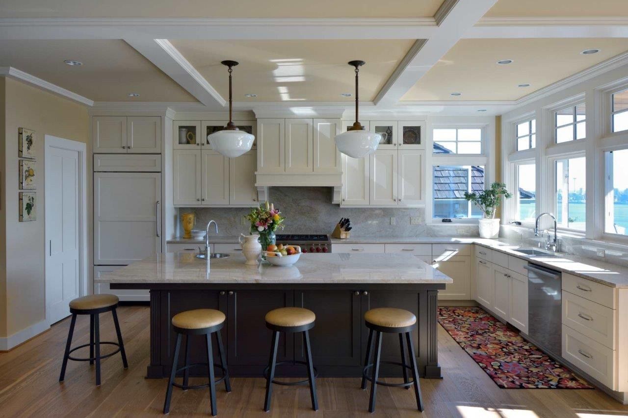 Bright kitchen with white cabinets, island stools, and large windows letting in sunlight