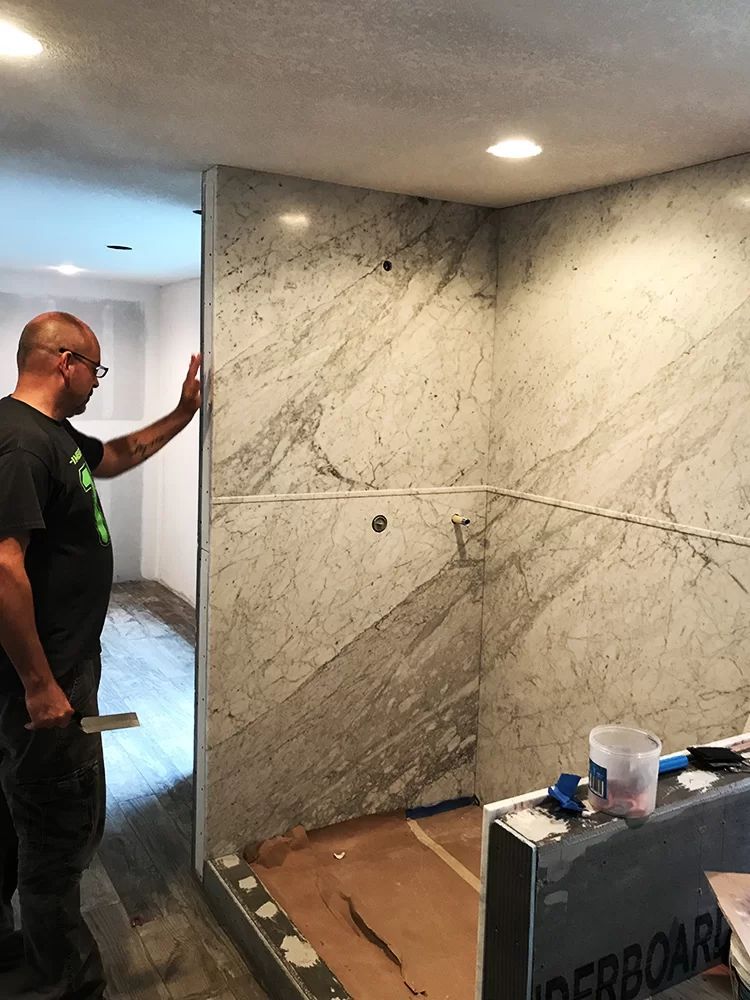 Man standing beside a marble shower wall during bathroom renovation with tools and materials nearby