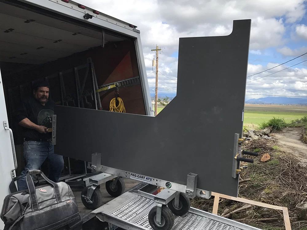 Man loading a large black panel into a truck at a rural site