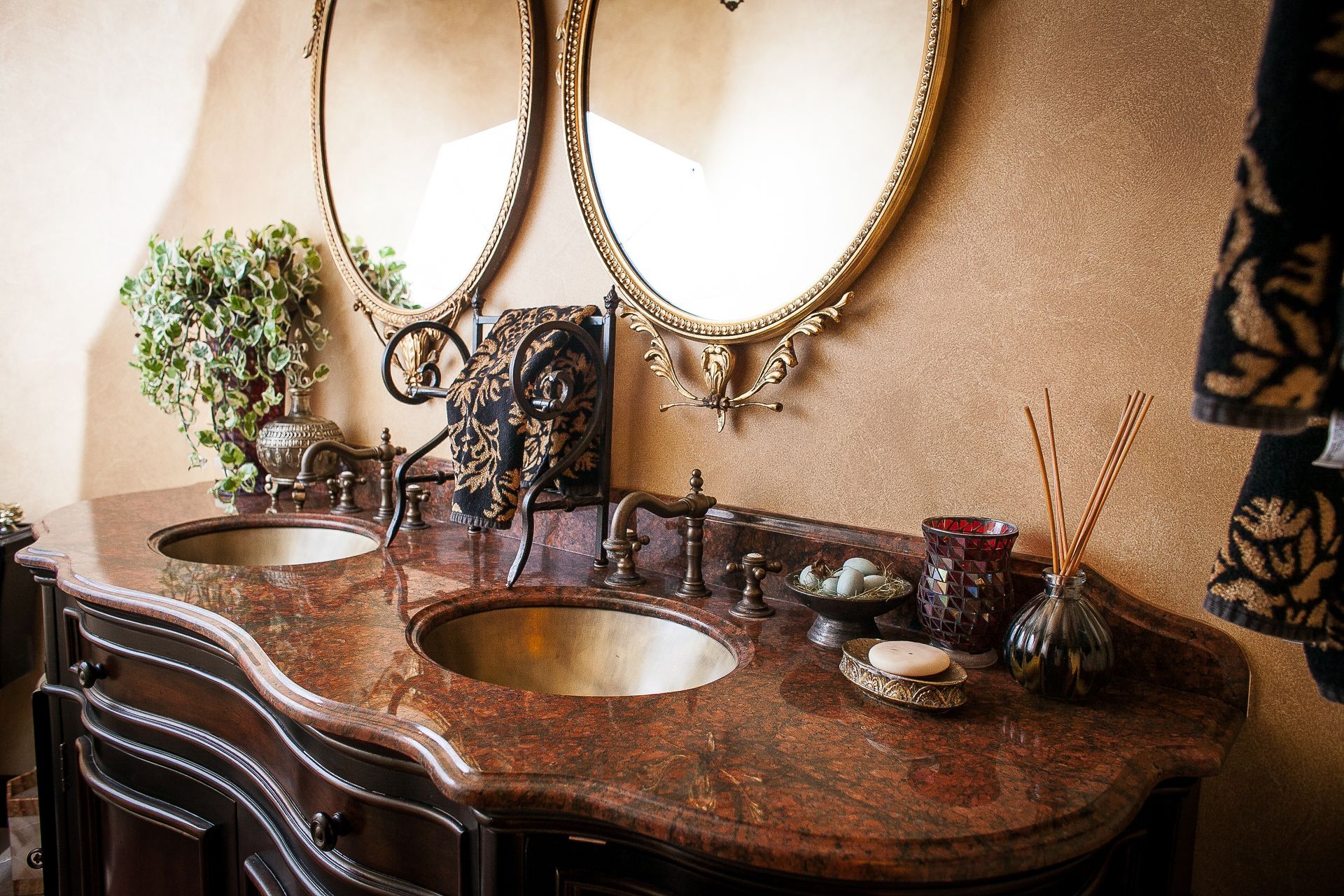 Ornate bathroom vanity with a copper sink, dark marble countertop, mirrors, and decorative candles