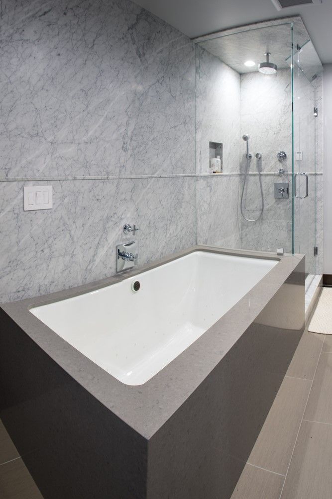 Modern bathroom with a freestanding white bathtub, gray marble walls, and glass shower enclosure.