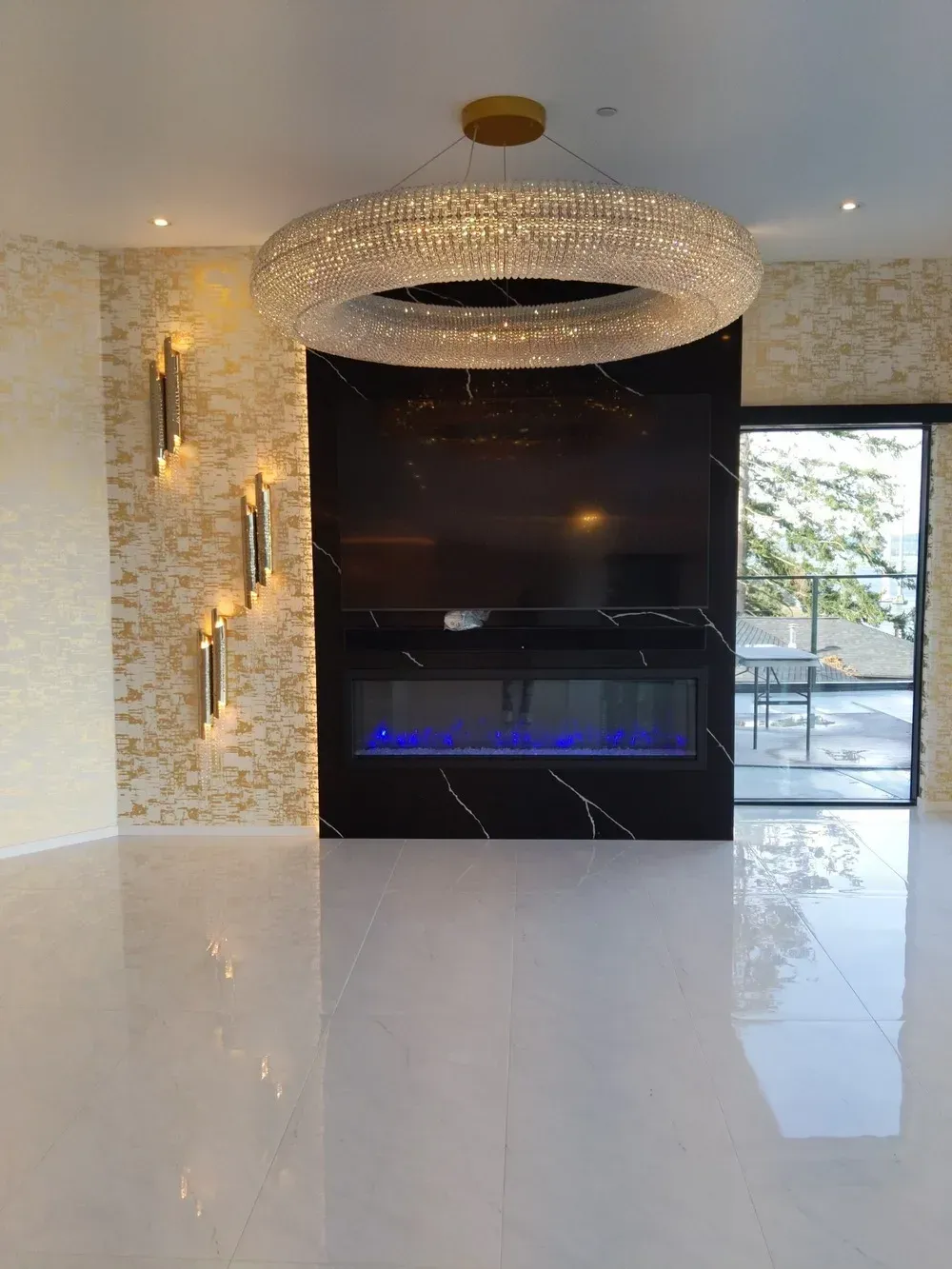 Modern living room with a black fireplace, crystal chandelier, wall sconces, and glossy tiled floor.
