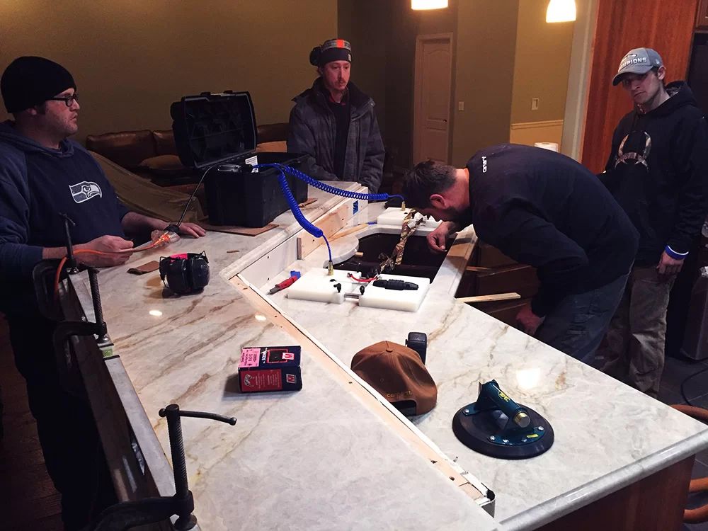 People around a long table assembling electronics with wires and tools in a workshop.
