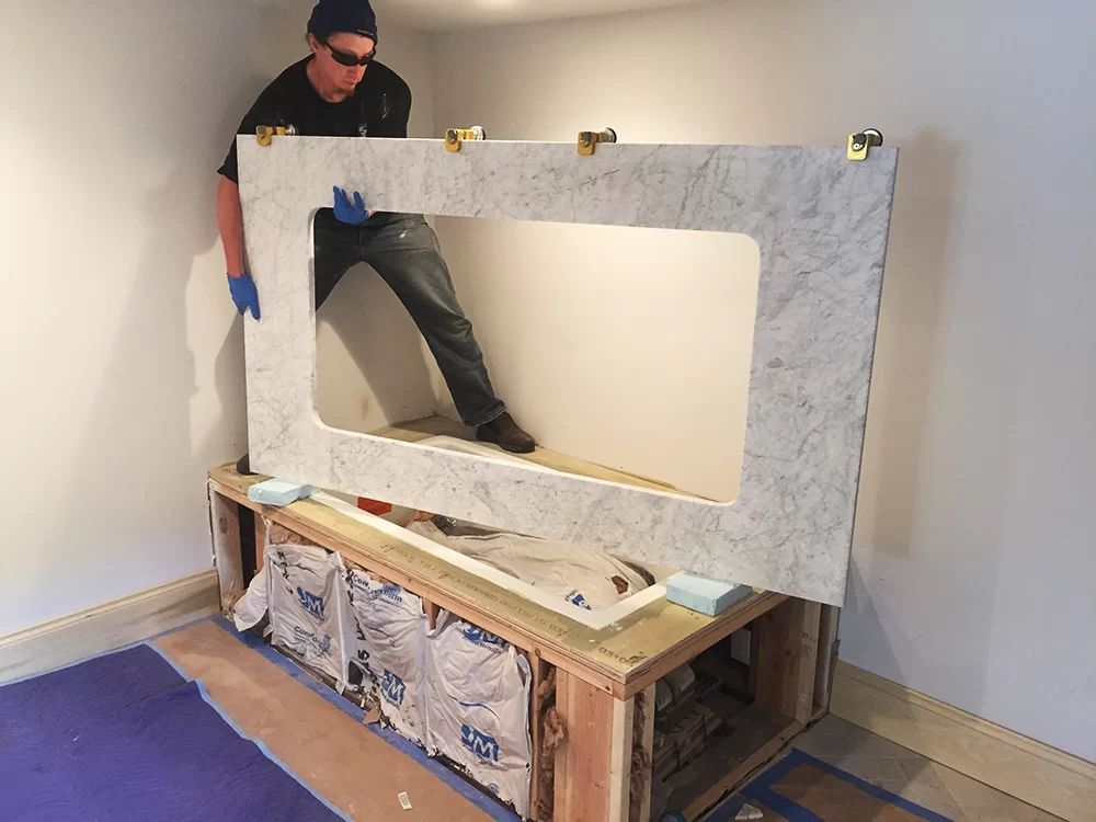 Person installing a large stone-look mantel frame over a built-in fireplace opening