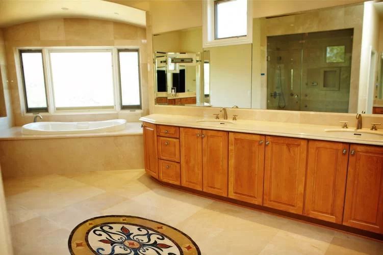 Bright bathroom with double vanity, large mirror, soaking tub, and a decorative floor medallion.