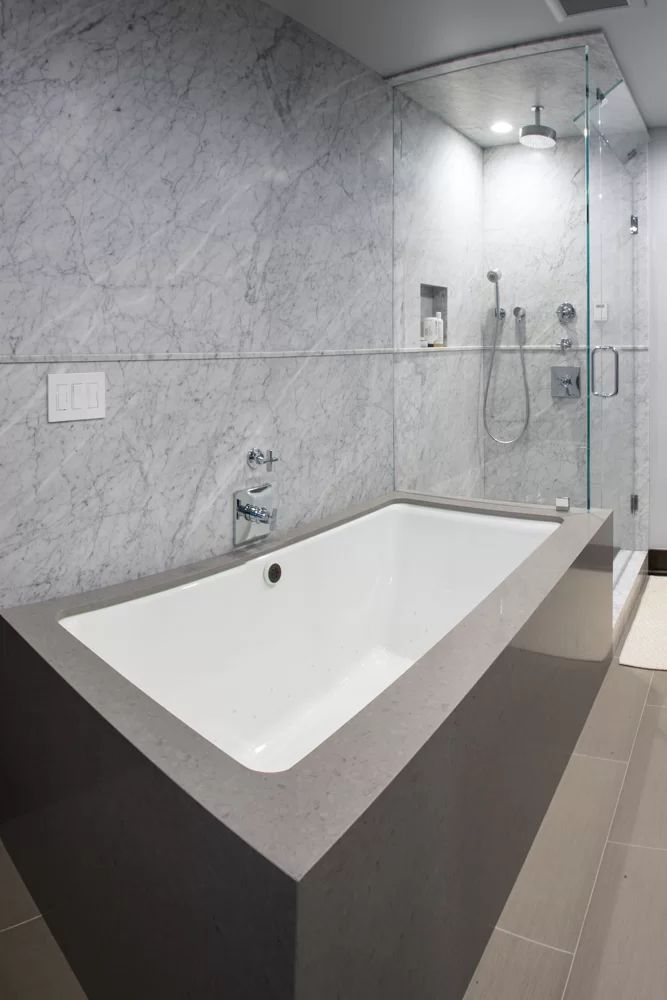 Modern bathroom with a white bathtub, marble walls, glass shower, and beige tile floor