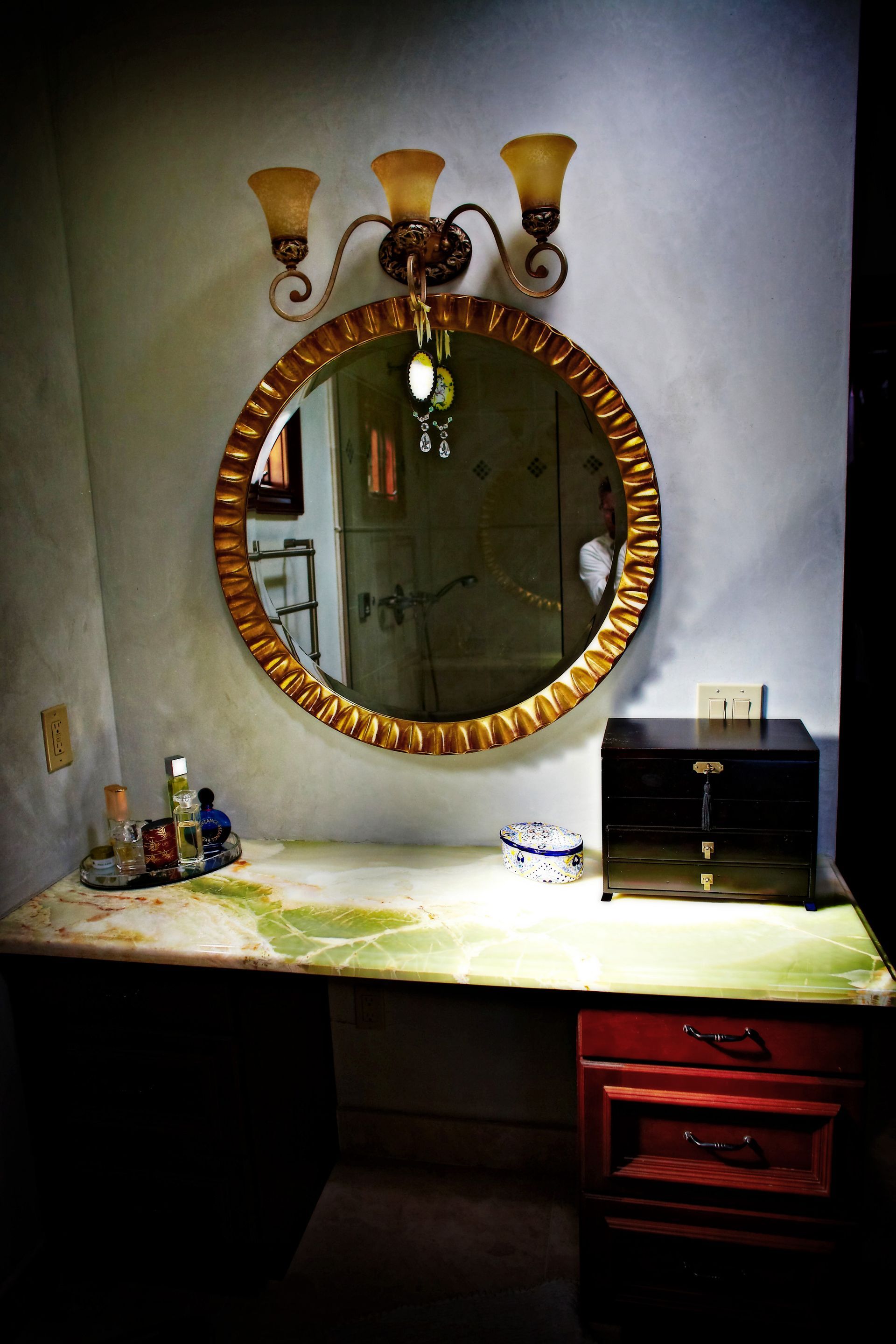 Vanity table with round mirror, wall sconce, and scattered toiletries in a dim room.