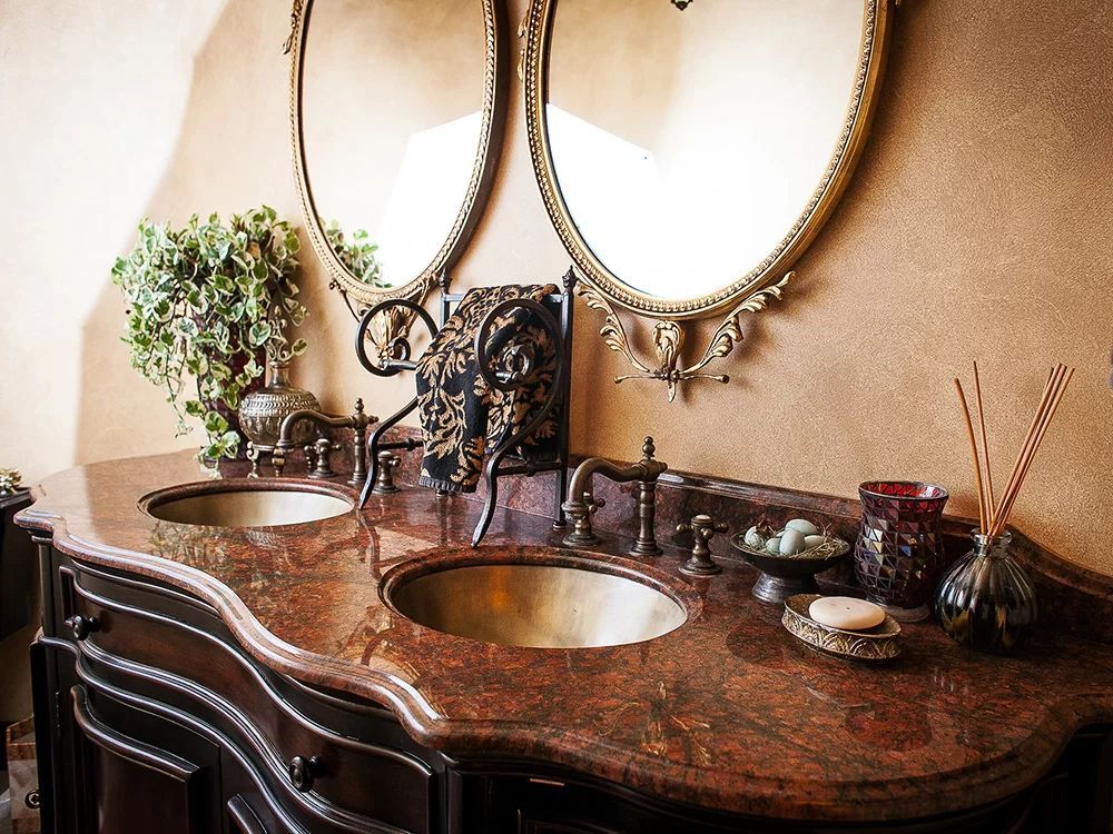 Elegant bathroom vanity with a marbled countertop, ornate sinks, and gold-framed mirrors