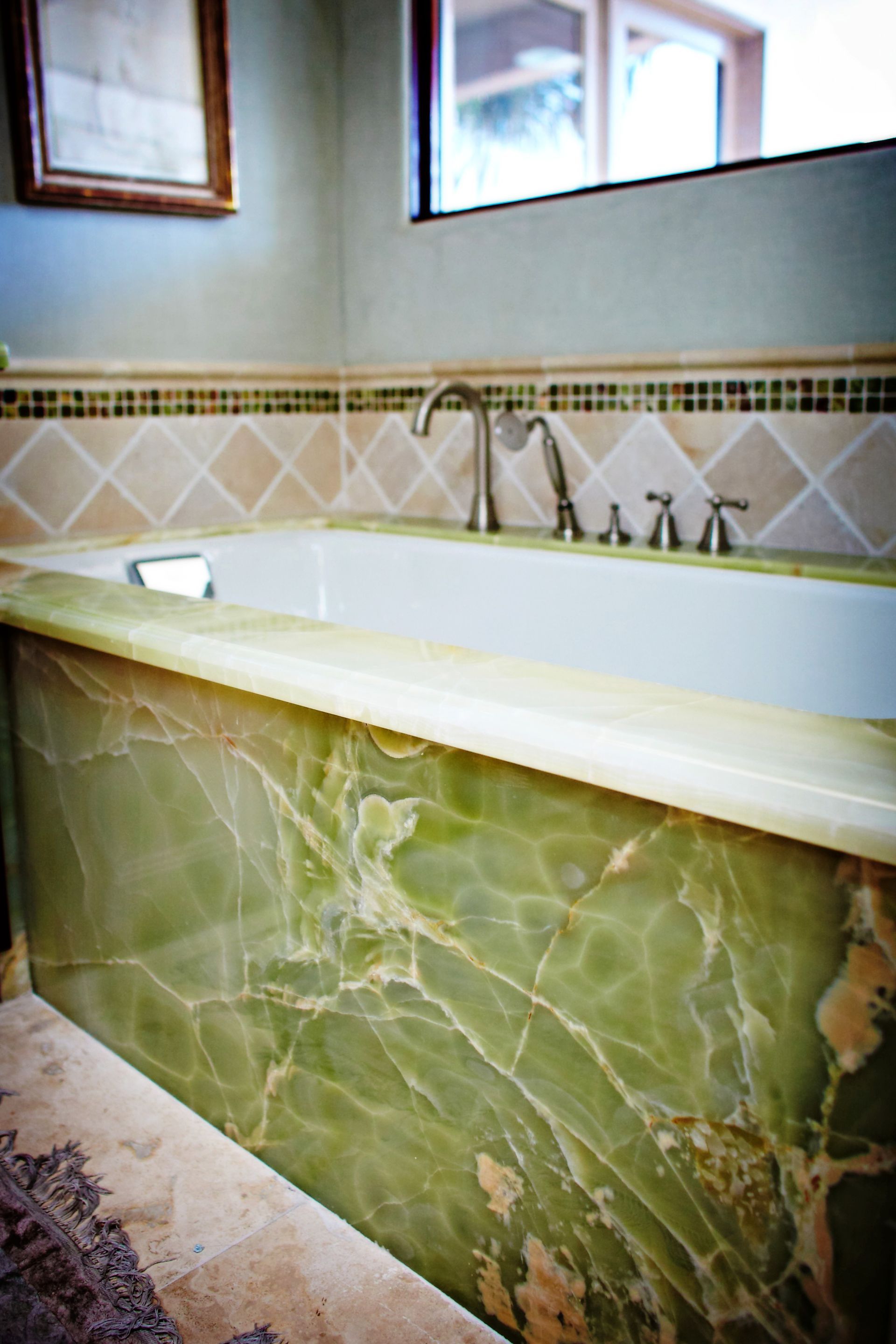 Green marble bathtub with white tile backsplash and wall mirror in a bathroom