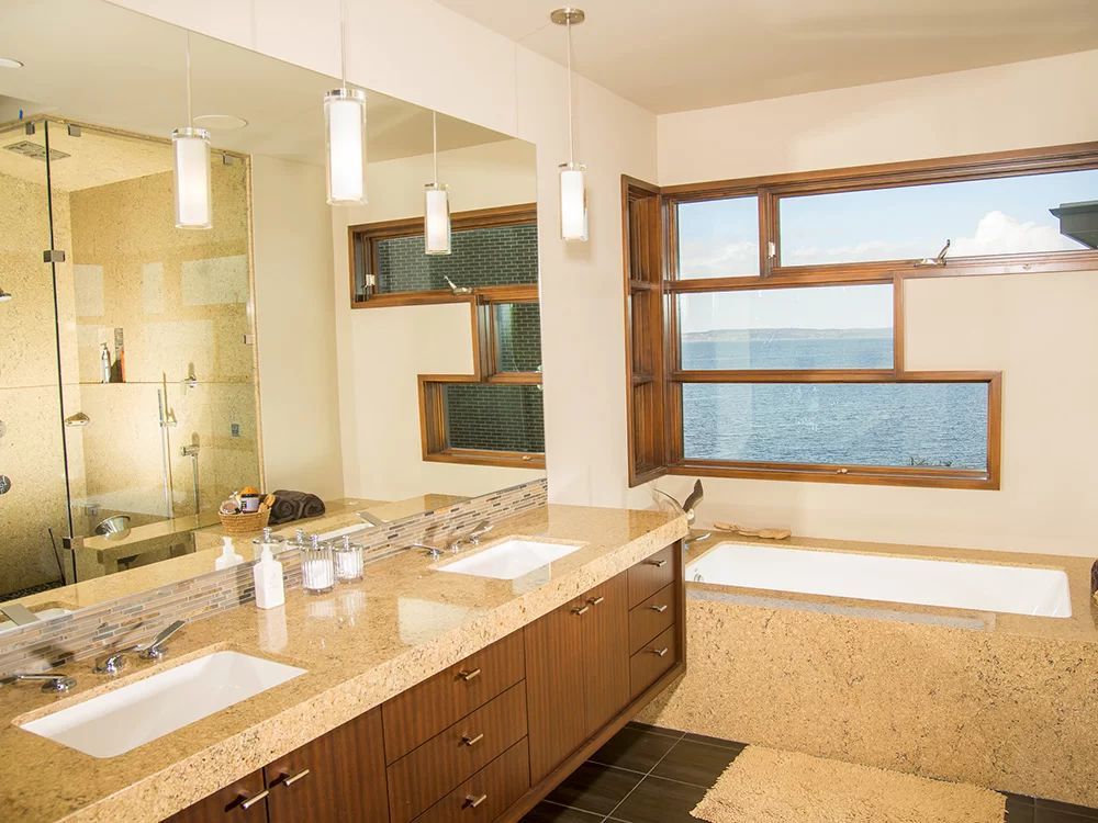 Modern bathroom with double vanity, large mirror, glass shower, and a soaking tub by a window.