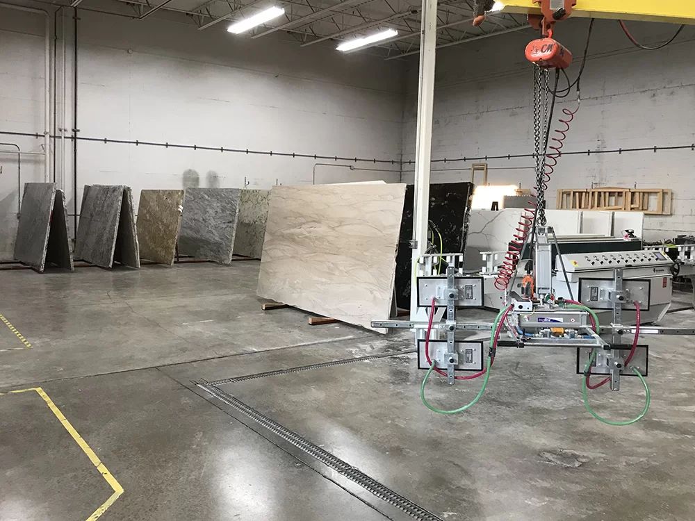 Industrial warehouse with large stone slabs and a suspended robotic lifting rig on a concrete floor