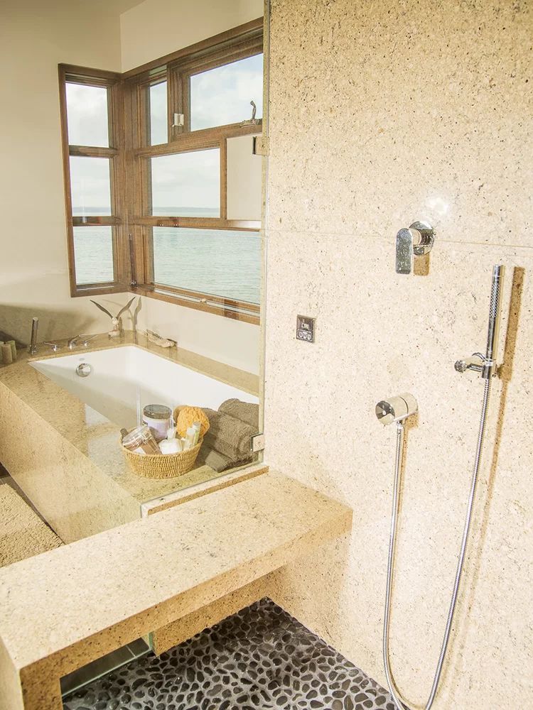 Spa-like bathroom with soaking tub, beige stone counters, and handheld shower on tiled wall
