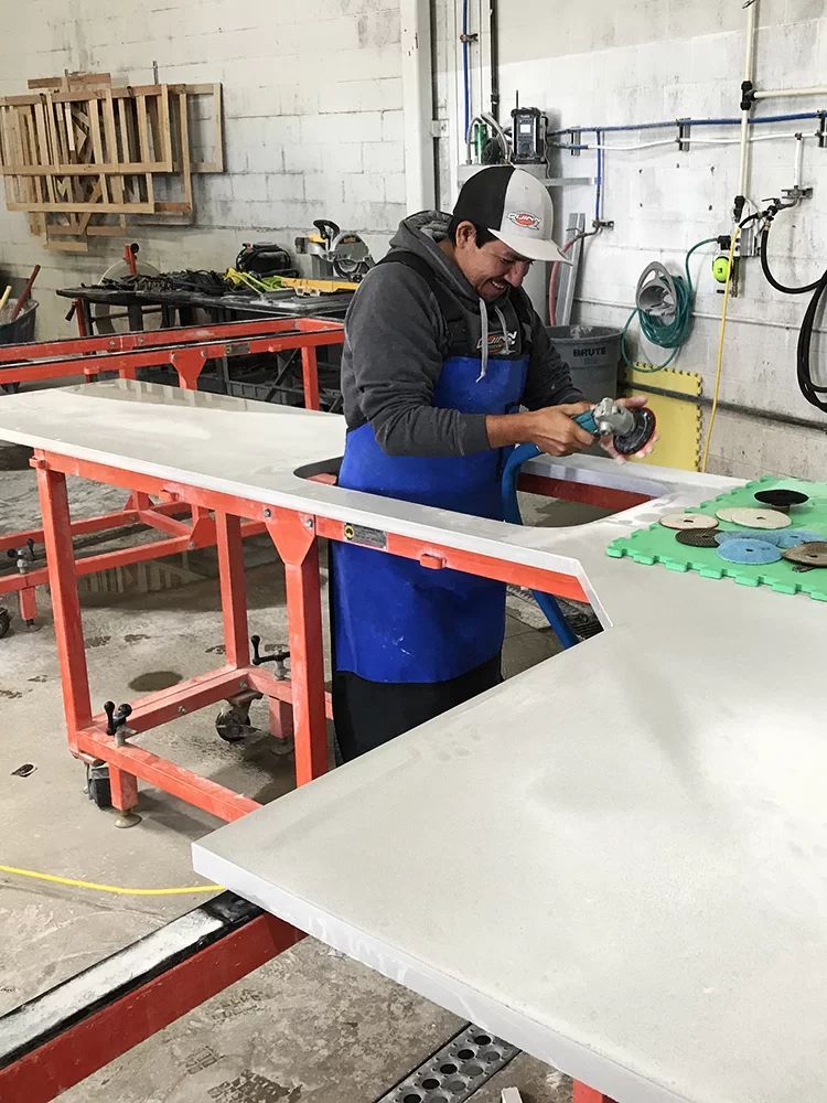 Worker sanding a white panel in a workshop with red metal tables and tools.