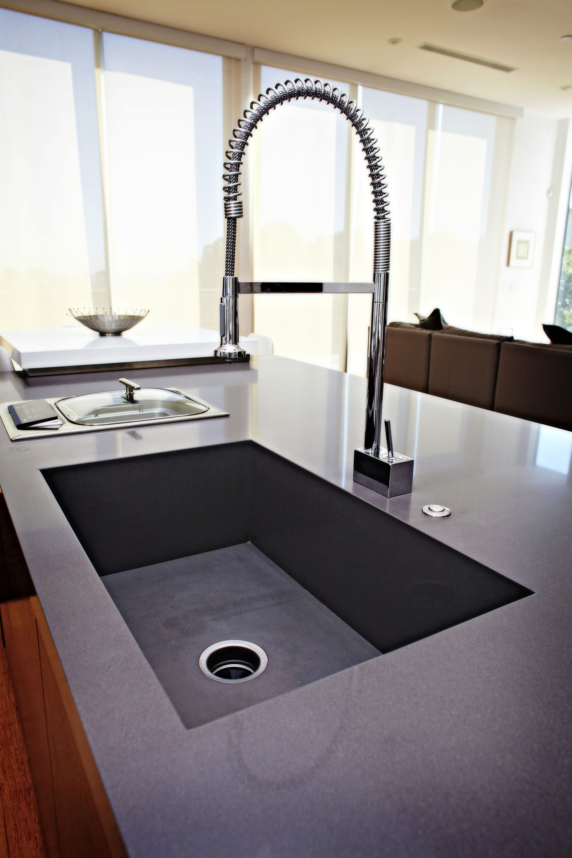Modern kitchen island with black countertop, deep sink, and tall chrome faucet near bright windows