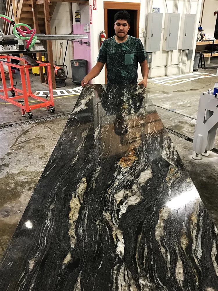 Person standing behind a large black-and-gold marble slab in a workshop