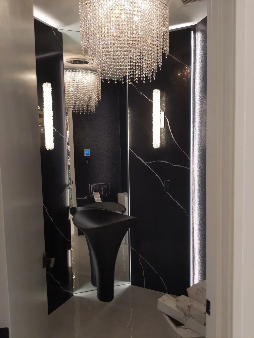 Luxurious black-and-white restroom with crystal chandeliers and a pedestal sink