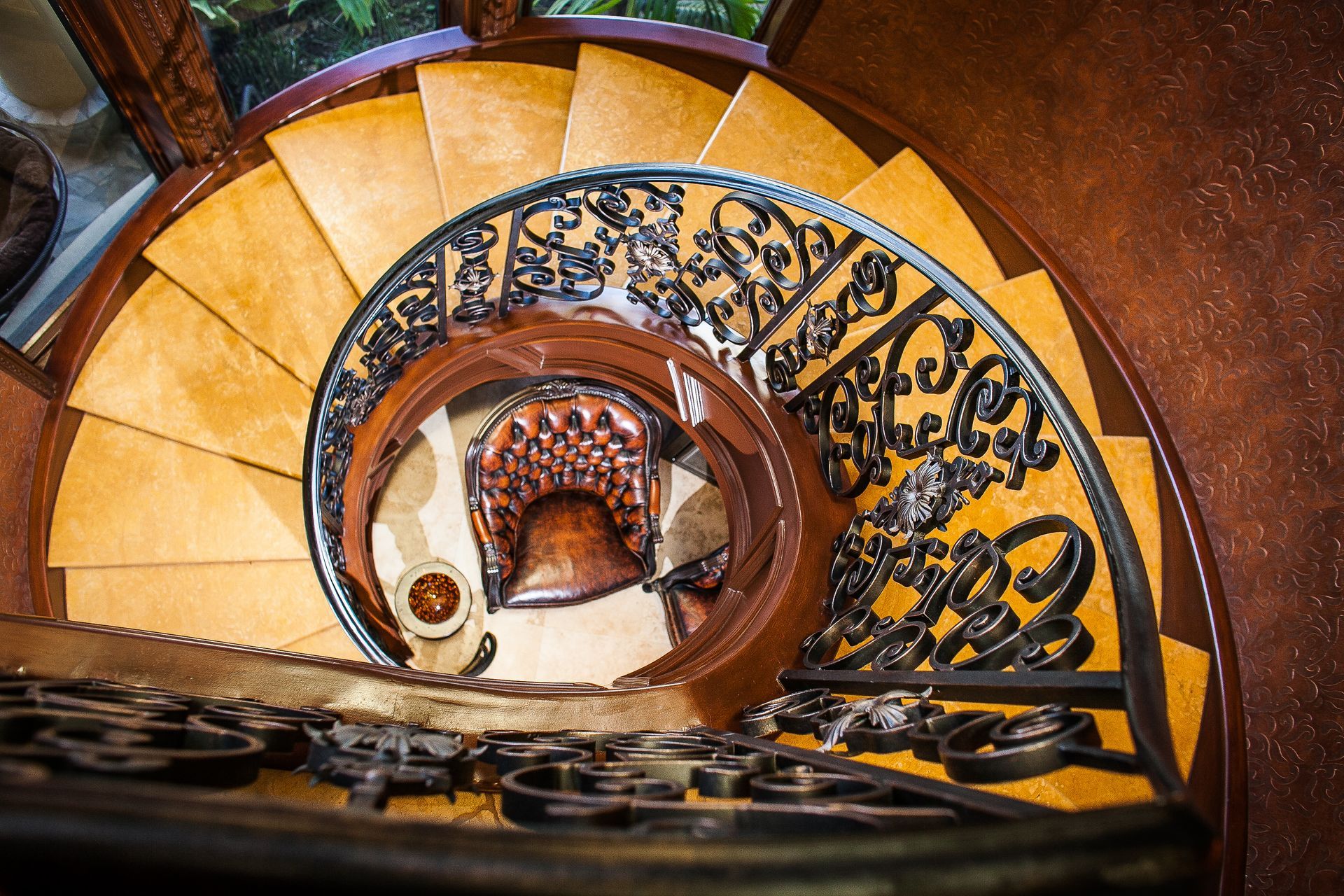 Spiral staircase with orange steps and ornate black iron railing, viewed from above.