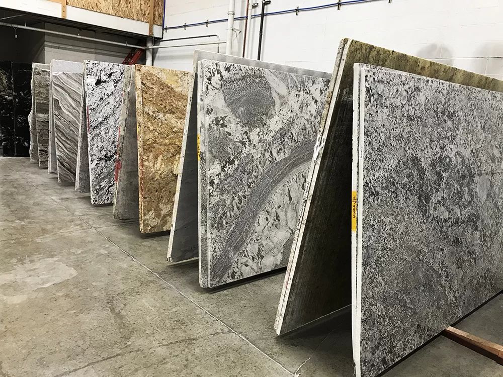 Large stone slabs displayed upright in a warehouse, showing gray and beige marble-like patterns.