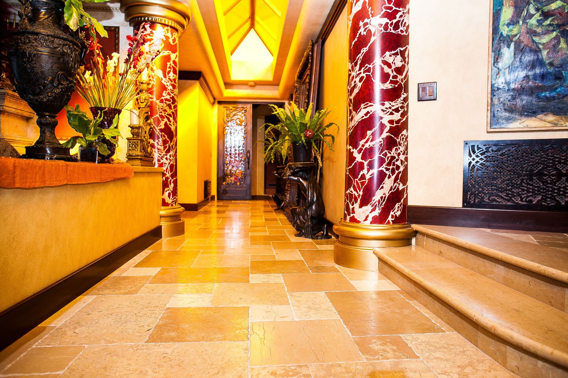 Warm-lit hotel hallway with marble floor, red columns, and decorative wall art