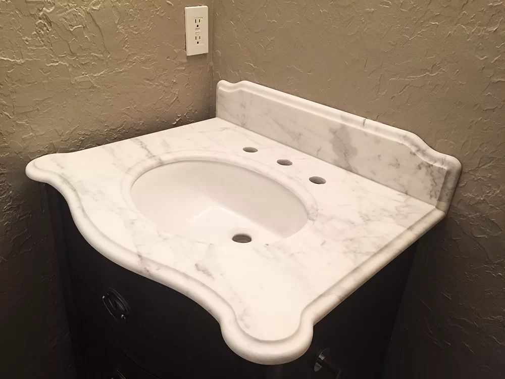 White marble bathroom vanity sink with backsplash and wall outlet in a corner.