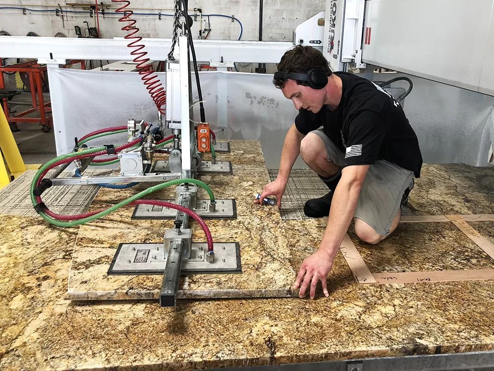 Man kneeling on a workbench, using tools and cables on a mottled wood surface in a workshop