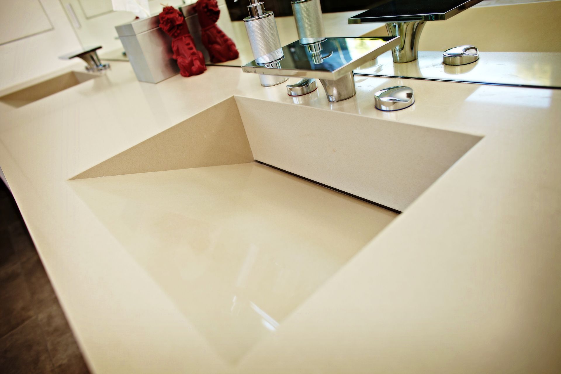 Modern bathroom sink with glossy white counter, chrome faucets, and a red towel in the background