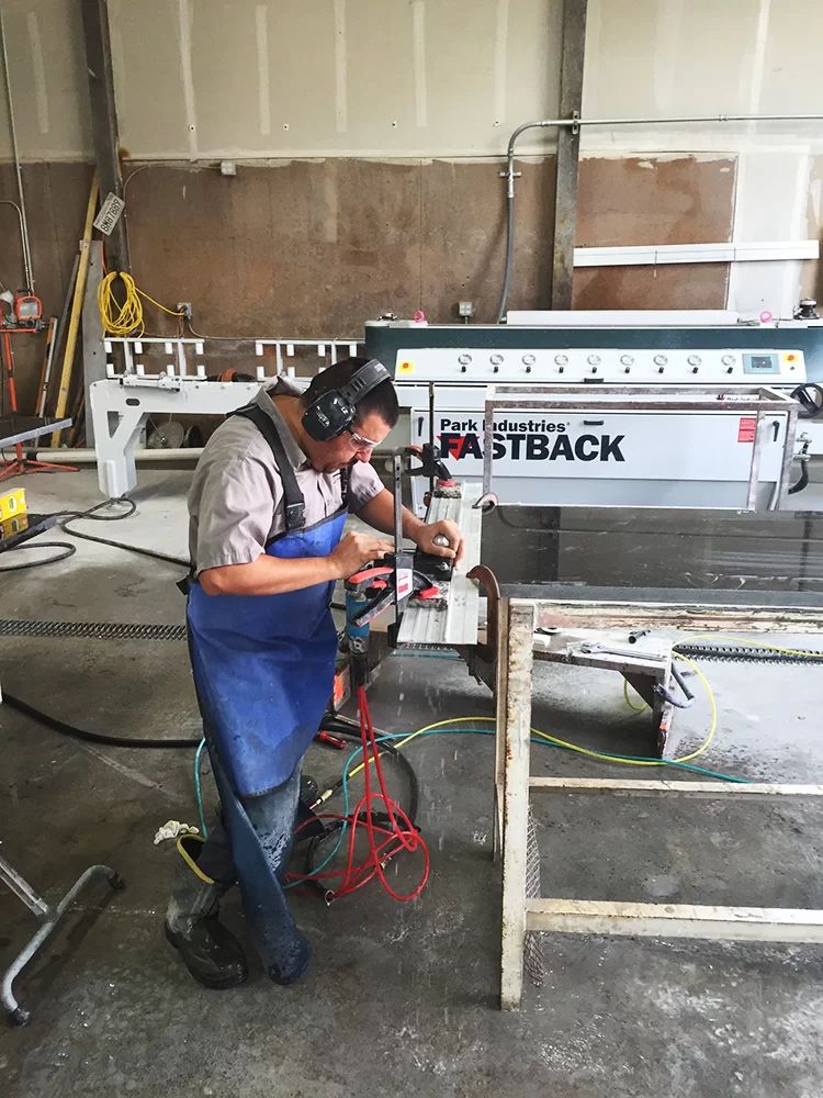 Worker using power tool in a garage workshop beside a metal machine and wooden frame