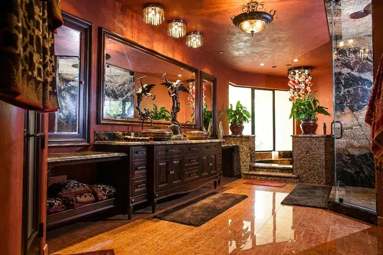Luxurious marble bathroom with double vanity, large mirror, warm lighting, and potted plants