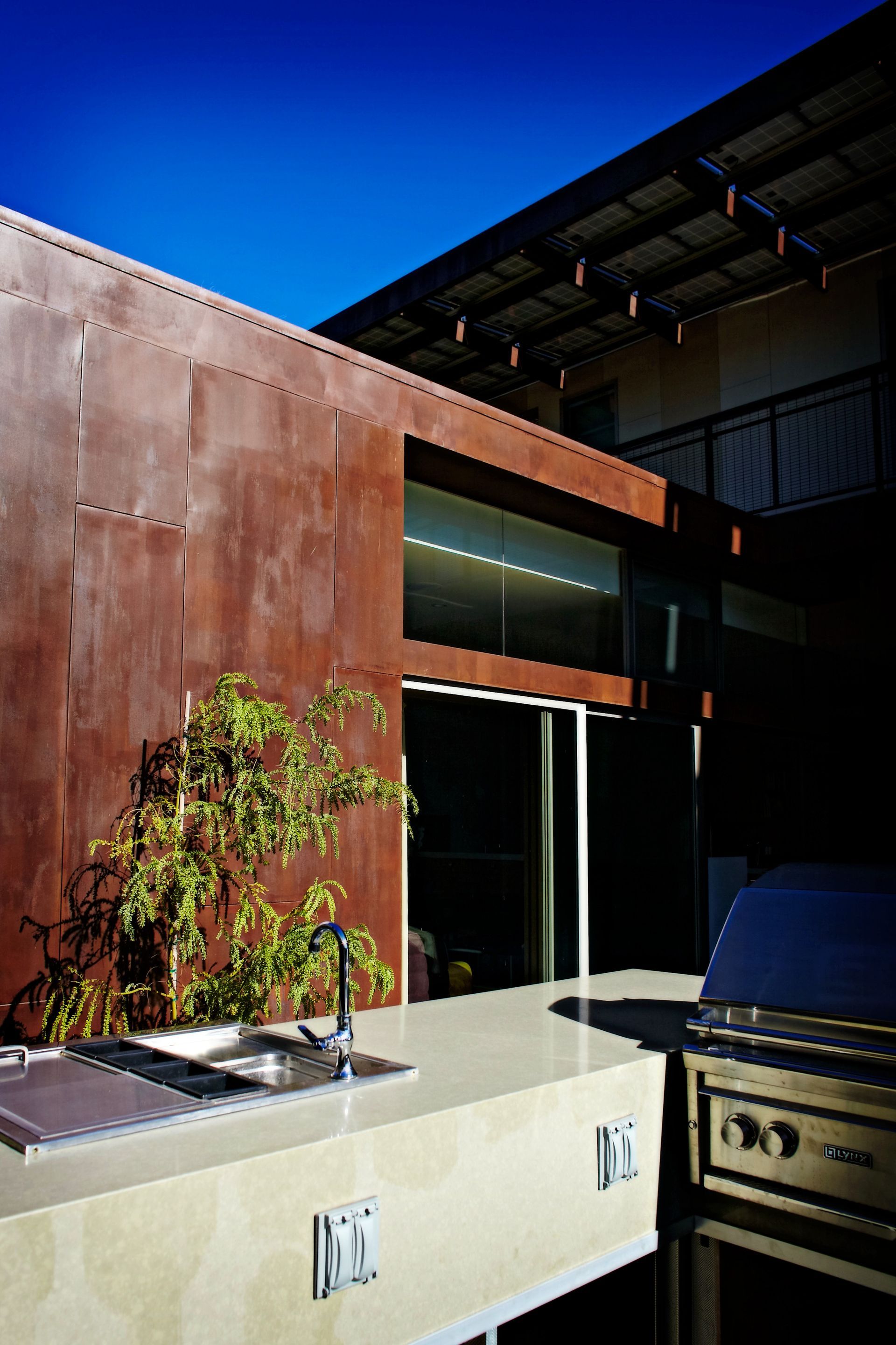 Outdoor patio with brick grill, concrete counter, and rust-colored wall under a blue sky