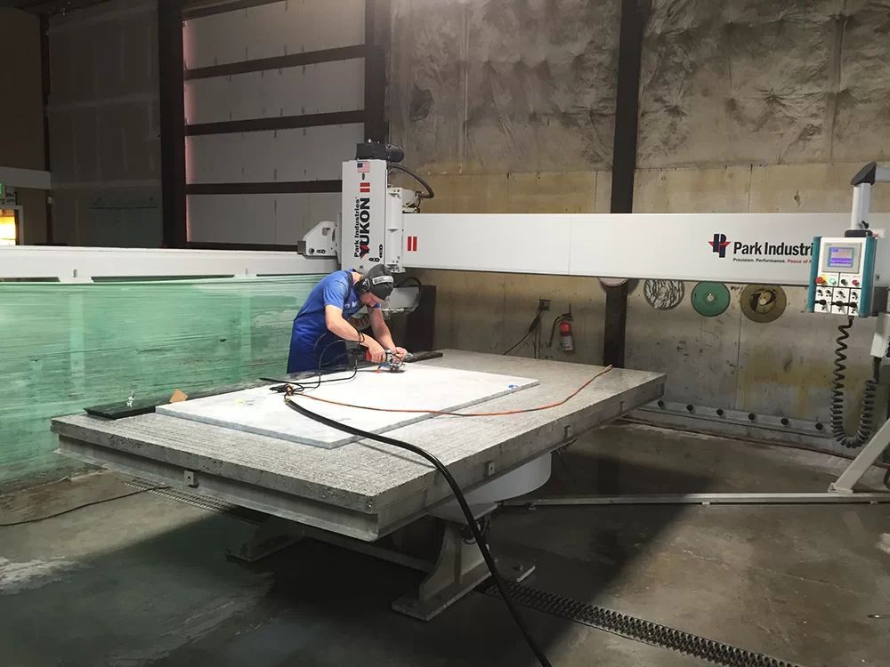 Worker using a large industrial machine to cut a white panel in a workshop