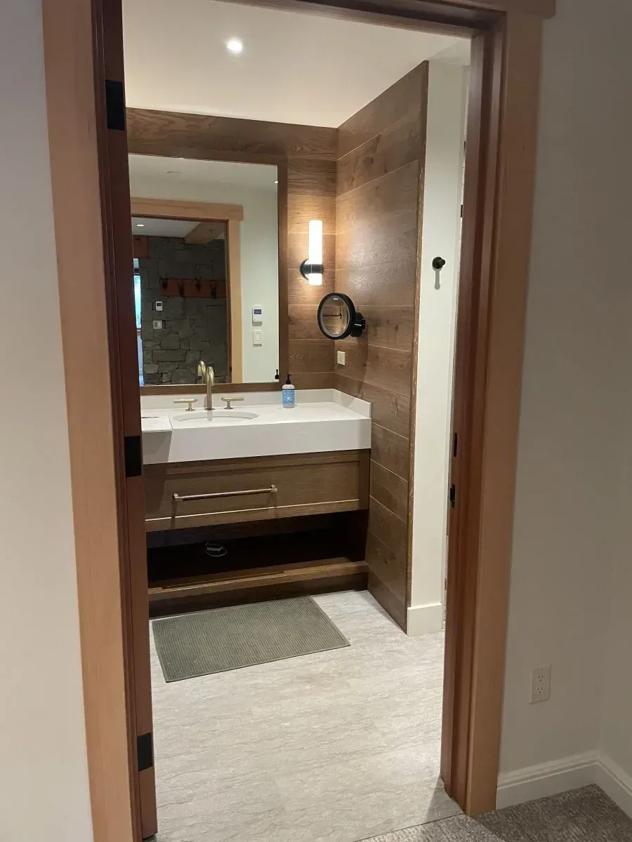 Bathroom vanity and mirror seen through an open doorway, with beige tile walls and a wall sconce.