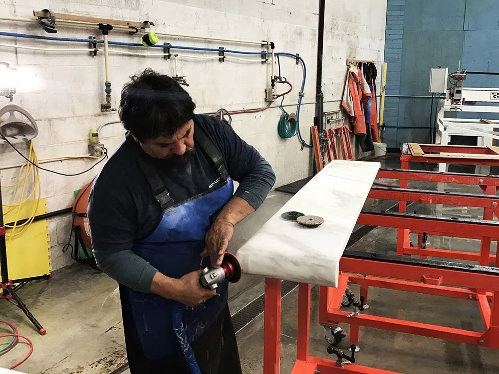 Worker in a blue apron sanding a white board on a red workbench in a workshop