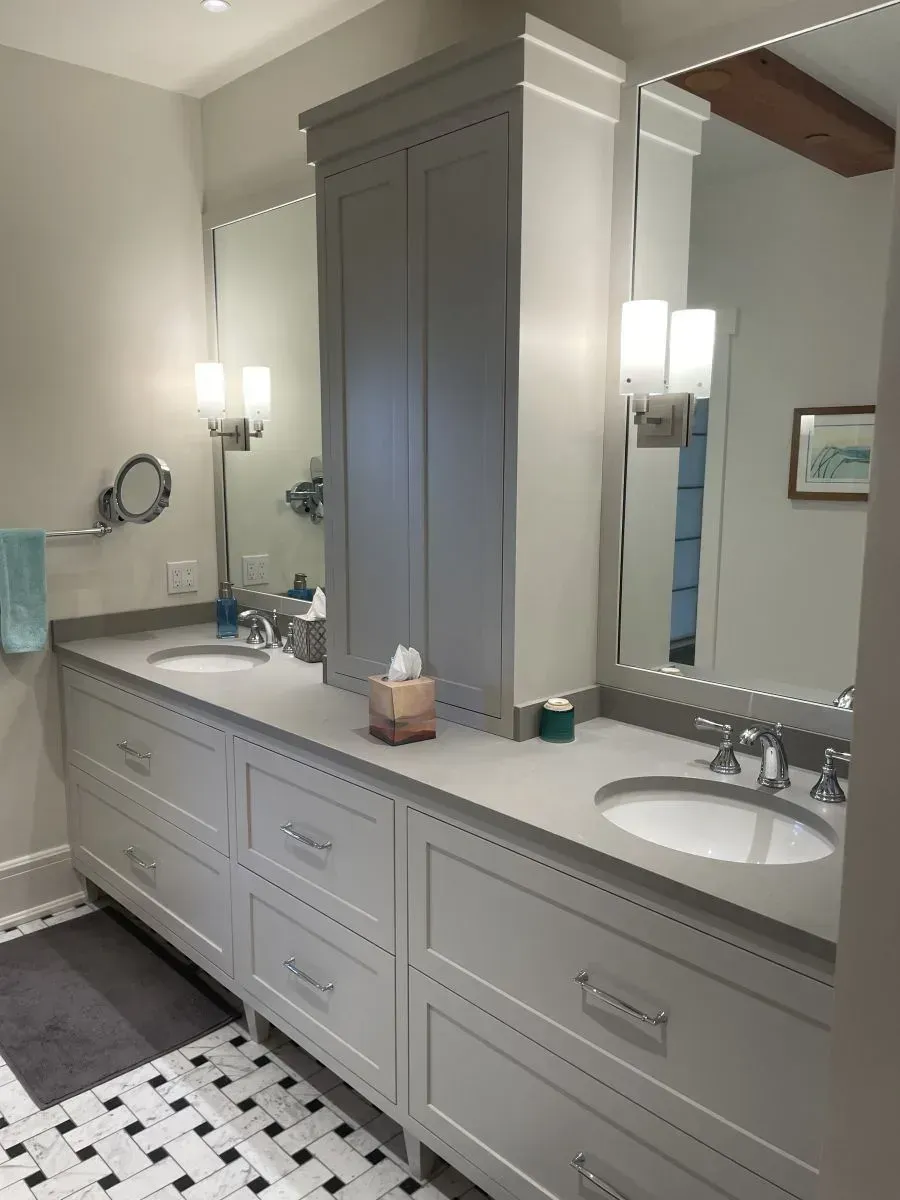 Bright bathroom with double vanity, gray cabinets, large mirror, and black-and-white tile floor
