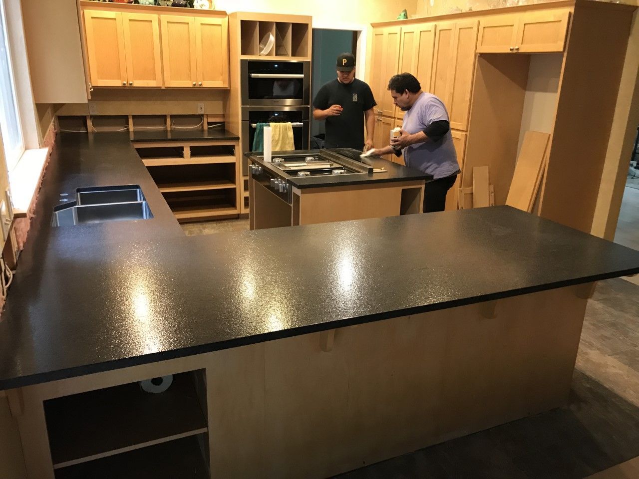 Two people installing a kitchen island in a wood-finished kitchen with black countertops.