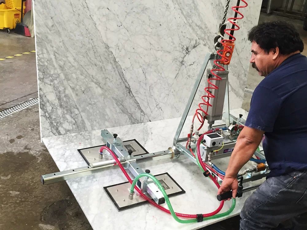 Worker operating a vacuum lifter to move a large marble slab in a workshop