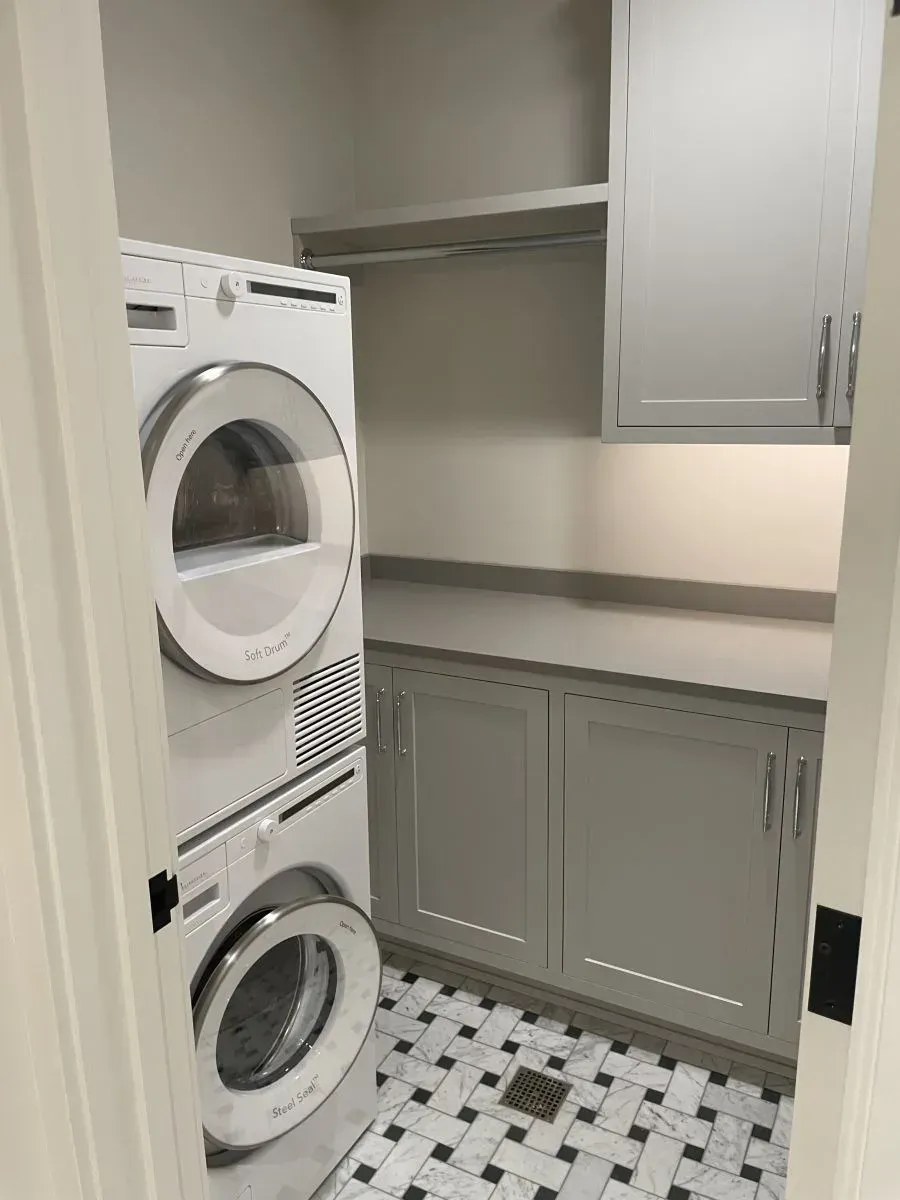 Laundry nook with stacked washer and dryer, gray cabinets, and black-and-white tiled floor.