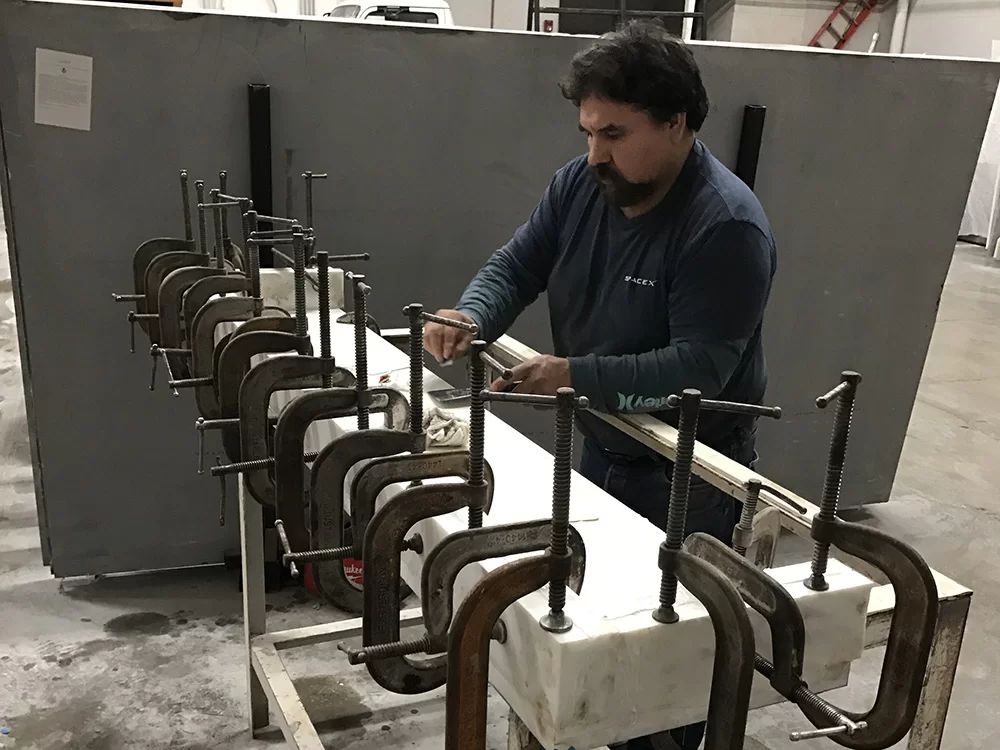 Worker tightening clamps on a white mold in a workshop, with large dark metal forms lined up nearby.